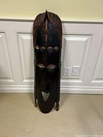 Front view of the tall dark wooden carved sculpture, showing facial features and reddish brown painted details.