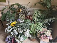 Overall display of artificial flowers and greenery including ferns and various pots and baskets, well lit with detail on leaves and flower shapes