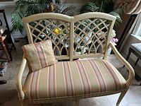 Front view of the loveseat style bench showing the wooden frame with lattice backrest and striped seat upholstery with matching pillow.