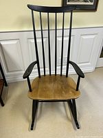 Black wooden rocking chair with seven vertical slats on backrest, curved armrests, and contoured wooden seat on rocking legs.