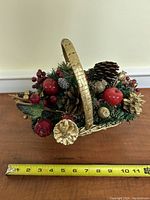 Top-down view of the decorative Christmas basket showing pine cones, red berries, small apples, and gold-painted elements with a tape measure showing approx. 11 inches long