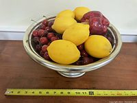 Photo shows a metal bowl approximately 10-11 inches in diameter filled with six large plastic lemons and many small plastic cherries.