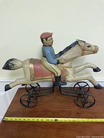 Side view of man on horse figurine mounted on wheeled metal frame, showing detailed paint and measuring tape for size reference.