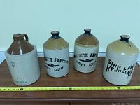 Photo of four pottery jars arranged in a row on a wooden surface with measuring tape showing approximately 10 inch height.