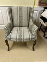 Front view of the small wingback chair showing patterned upholstery, padded arms, and wooden cabriole legs.