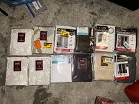 Overview of 12 sealed curtain bundles laid out on the floor, showing brand labels and colors.