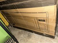 Closed cardboard box with illustration and model number MC0165UW, showing the microwave oven front and control panel design.