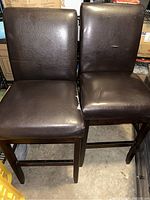 Two chocolate dark leather swivel bar stools shown side by side, showing the padded seats and backs with scratches.