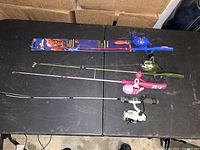 Four kids fishing rods with reels on a black table, clearly showing the Spider-Man fishing rod and the other three colorful rods.