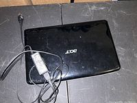 Closed black Acer laptop with visible Acer logo on lid and attached charger cable.