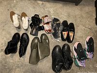 View of 9 pairs of shoes arranged on concrete floor, showing a variety of styles and colors.
