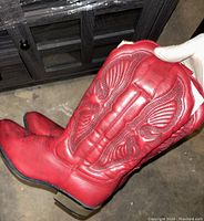 Close-up side view of red cowboy boot showing raised wing and feather decorative stitching and sole condition.