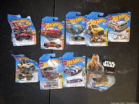 High resolution photo of the nine Hot Wheels cars in original packaging laid out on a dark surface, showing vehicle details and card artwork.