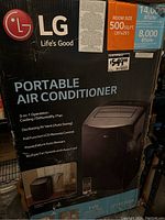Front of the original product box showing LG Portable Air Conditioner branding, features, and specifications including 14,000 BTU/hr cooling, 8,000 BTU/hr dehumidifying, and room size coverage of 500 sq. ft.