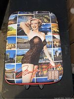 Front angled view showing the image of Marilyn Monroe in a black swimsuit with scenic landmark collage background on the front of the suitcase.