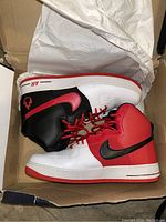 Pair of Nike high-top sneakers inside a box, viewed from the side showing color details and laces.