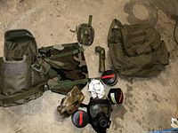 Overview photo showing three military bags, gas mask, filters, flashlight and tape on concrete floor
