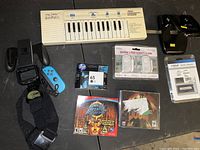 Overview of all items laid out on a black surface showing various electronics, gaming accessories, security alarms, and PC games.