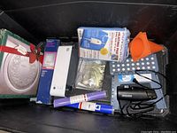 Various home items in a bin including kitchen tools, electronic accessories, and household goods, mostly new or lightly used