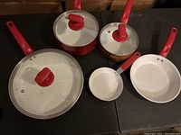 Five-piece cookware set with red handles and white interiors including two saucepans with lids, two frying pans of different sizes.
