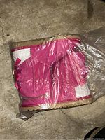 Side view of a pink UGG boot in plastic wrapping showing the Velcro straps and boot design