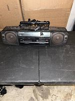 Panasonic Express-FT500 vintage boombox radio cassette front side with power cord on top, placed on black surface with brown cardboard boxes behind.