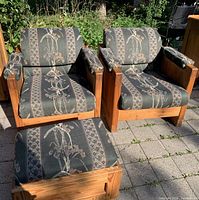 Two solid pine framed armchairs and one ottoman outdoors on patio paving. Chairs and ottoman upholstered in green fabric with floral and geometric pattern.