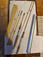 Photo showing two vintage fishing rods disassembled into multiple sections along with a yellow canvas sleeve and a metal carrying case.