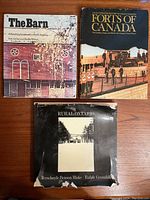 Three books displayed on wooden floor: 'The Barn', 'Forts of Canada', and 'Rural Ontario' with visible wear and tear on the covers.