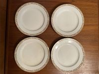 Four white plates arranged in a square, showing overall shape and size with subtle gold and pink floral decorative border