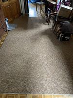 Photo of a large rectangular area rug laid out on a floor, showing its full length and speckled pattern in neutral brown and beige tones.