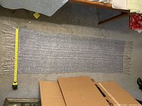 Full image of gray hand woven runner rug with measuring tape showing length.