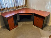 Front and side view of L-shaped workstation desk showing wood-finish top, cupboard with disc storage, and drawers.