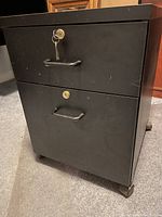 Front view of black metal two-drawer rolling cabinet showing locked drawers and handles.