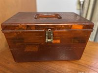 Closed amber plastic sewing box with latch and handle on wooden surface.