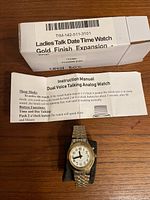 Original box and instruction manual for the talking watch alongside the watch displayed on a black foam holder.