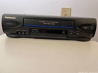 Front view of Panasonic VHS player showing model name, buttons, and jacks.