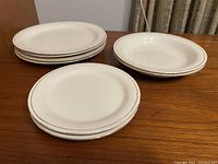 Stack of 4 large plates with gold rim on wooden surface