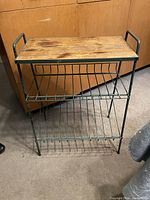 Front view of used wire stand with wire shelves and wooden top surface, showing metal frame and side handles.