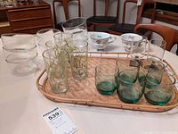 Photo of all glassware and cups arranged on a table, including Baileys cups, bamboo themed glasses, blue colored juice glasses, clear cereal bowls, and rattan tray