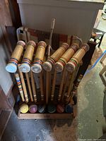 Front view of vintage wooden croquet set with six mallets and six colored balls in a wooden stand on floor.