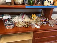 Full lot showing ceramic ashtray, brass and stone candle holders, candles, essential oils, and Italian pottery container on wooden shelf