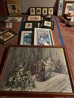Overview of numerous framed floral prints and needlework pieces laid on floor with a variety of frame styles and sizes.