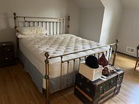 Full view of king size metal bed with mattress and bedding showing headboard, footboard, and rails in gold-tone metal finish with decorative finials on corners.