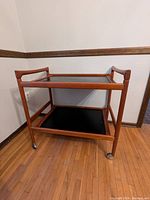Three-quarter view of two-tier teak serving cart against wall