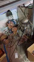 Full view of metal cat on bicycle, man with pail, metal frog, and flower spikes in basement setting