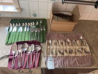 Full view of unfolded flatware including knives, forks, spoons, serving pieces laid out in fabric holders and in box