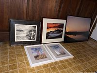 Lot contents showing two framed photos standing upright and three unframed prints laid flat on floor. Various maritime and nature themes.