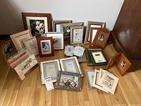 Lot of assorted picture frames arranged on floor against wall, showing variety of wood and metal frames in multiple sizes with some photos inside.