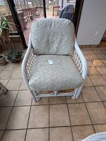 Front view of white rattan armchair with full cushions set on tiled floor indoors, cushions appear lightly used.